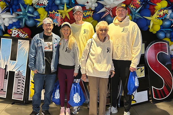 Kathy Brothers and several team members posing in front of a giant heroes sign.